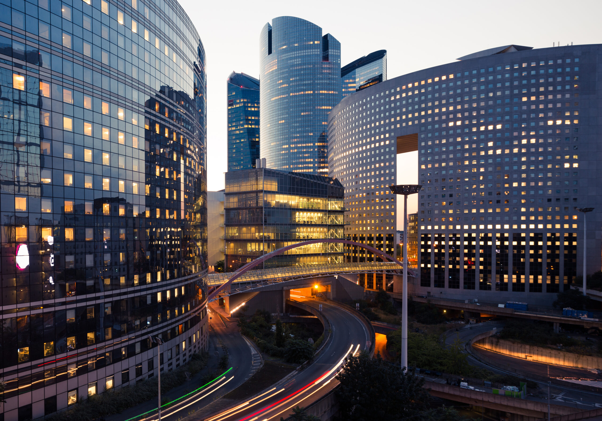 Skyscrapers in Paris business district La Defense. European night cityscape with dynamic street traffic, car lights and glass facades of modern buildings. Economy, finances, transport concept. Toned