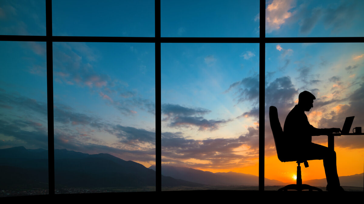 The man working at the table near a window on a mountain sunset background